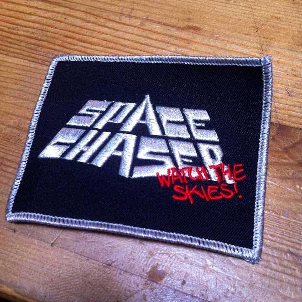 Space Chaser - Watch Patch <p>Macht sich mit feschem Silberfaden gut auf jeder Kutte!
100% Baumwolle - Grösse: 10x6 cm</p>